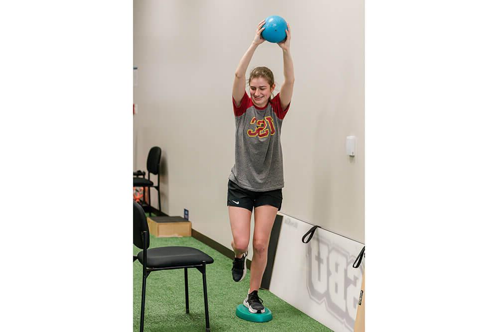 Physical therapy female student doing exercise lifting medicine ball above her head