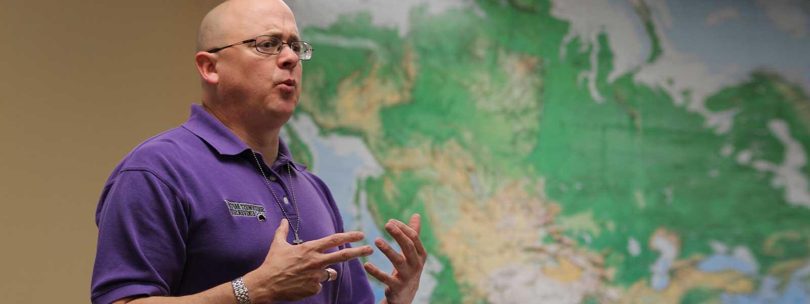 professor lectures in front of large wall map